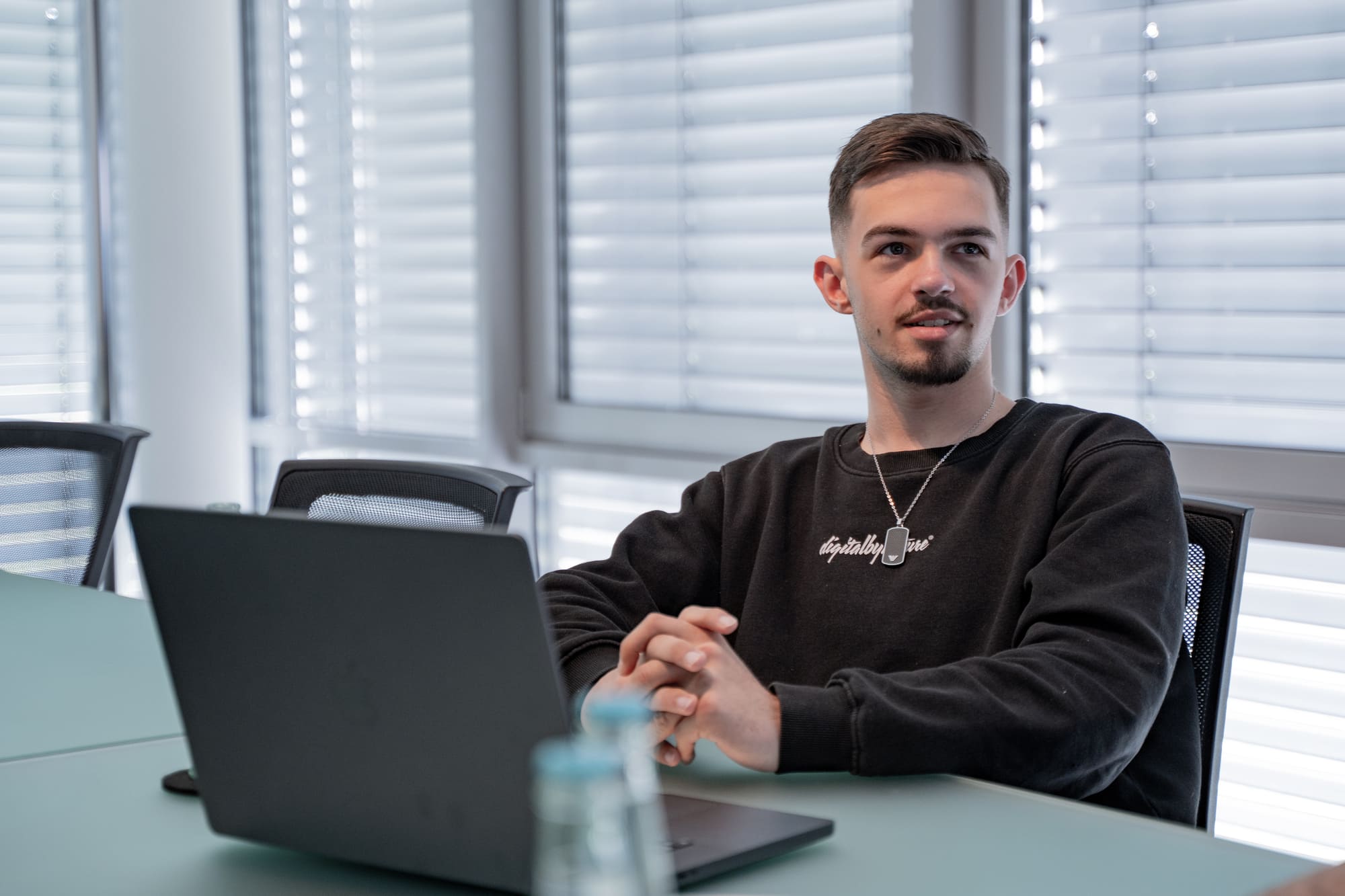 Joel von digitalbynaturedigitalbynature® im Meetingraum am Laptop, mit digitalbynature-Pullover