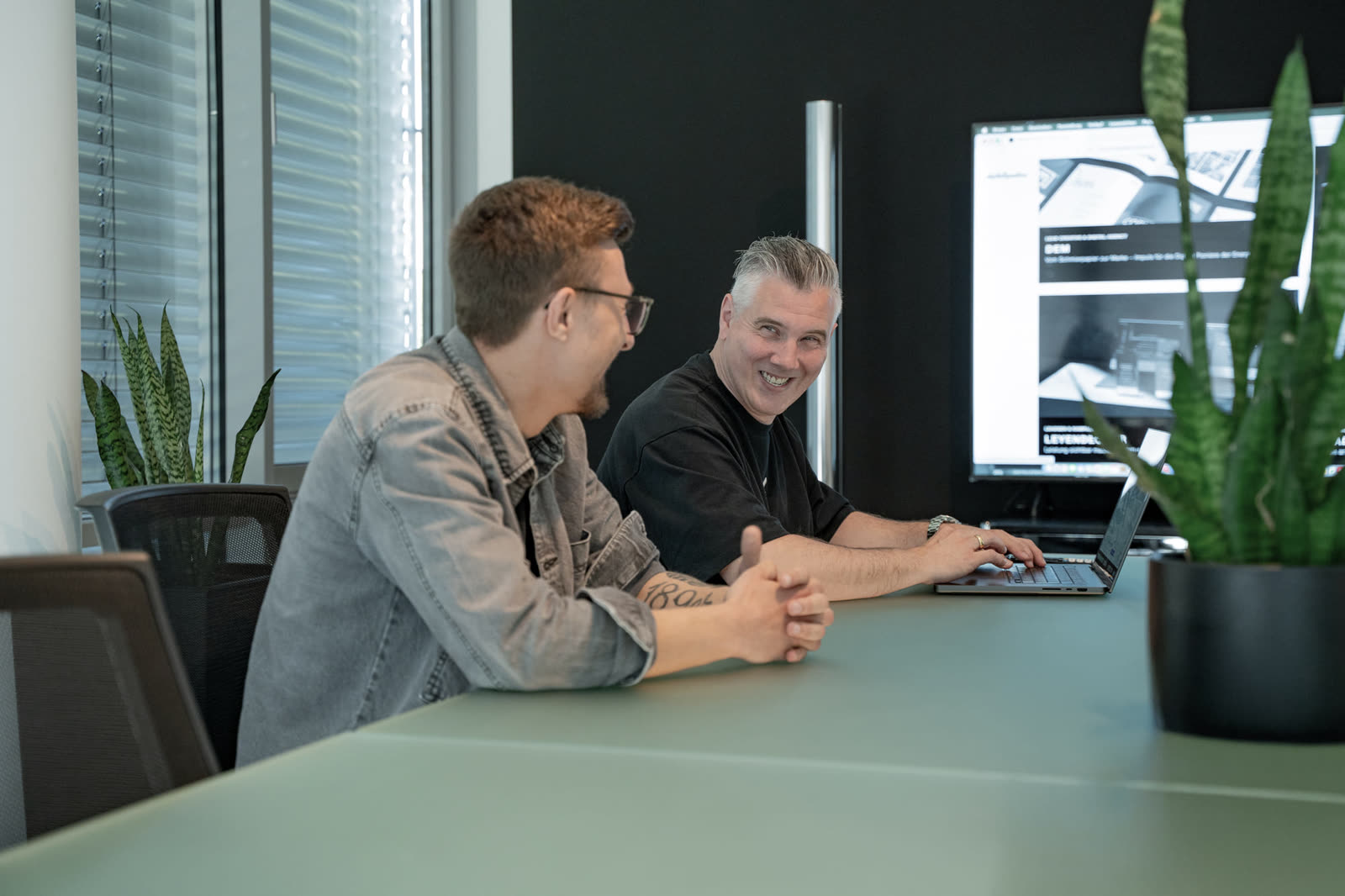 Pascal und Markus von digitalbynature® lachen bei der gemeinsamen Arbeit am Konferenztisch
